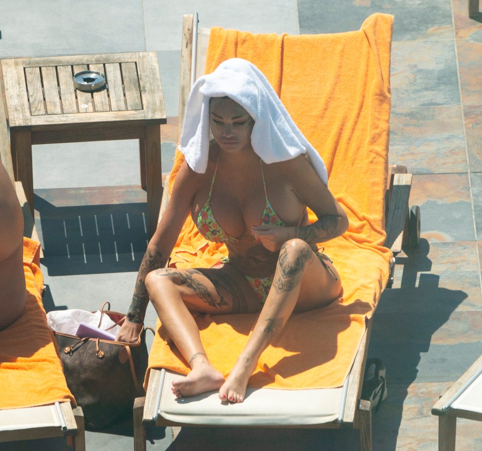 a woman in a bikini sits on a lounge chair with a towel over her head