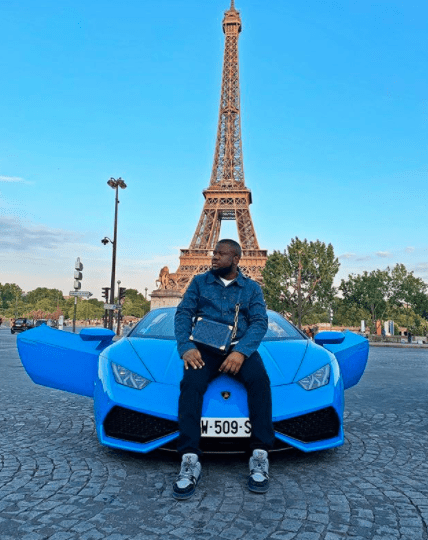 a man sits on the hood of a blue car with the eiffel tower in the background