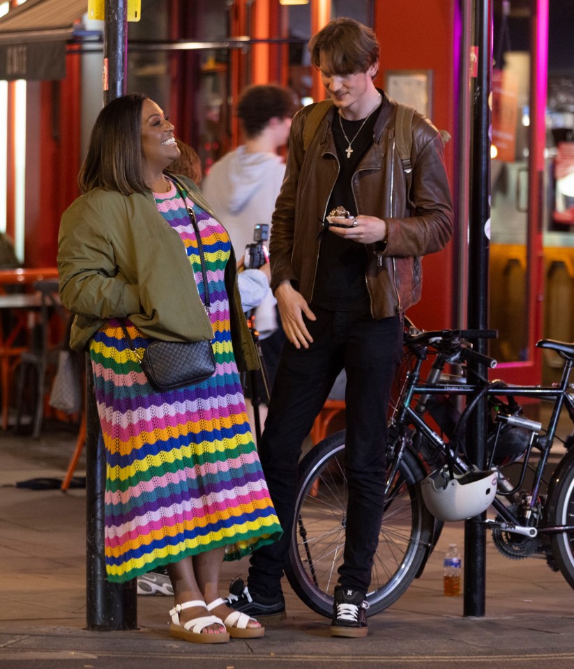 a woman in a rainbow dress stands next to a man in a brown jacket