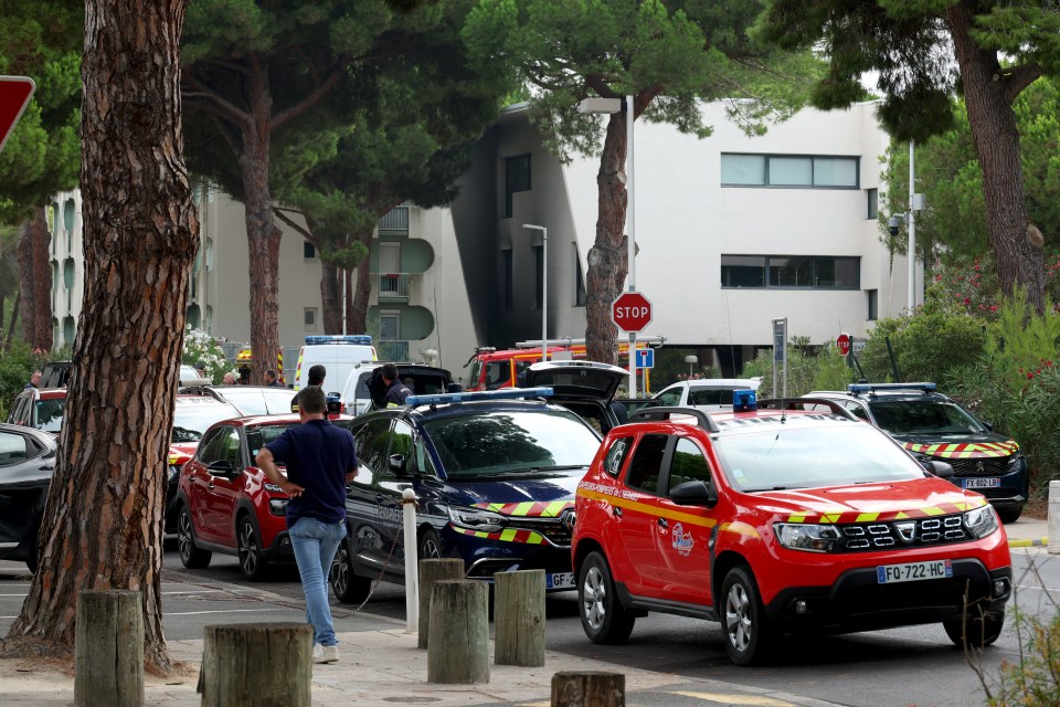 Law enforcement officers and firefighters stand in front of the synagogue building following the fire and explosion of cars in La Grande-Motte