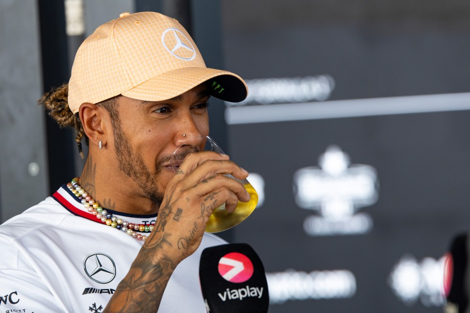 a man wearing a mercedes hat is drinking from a glass