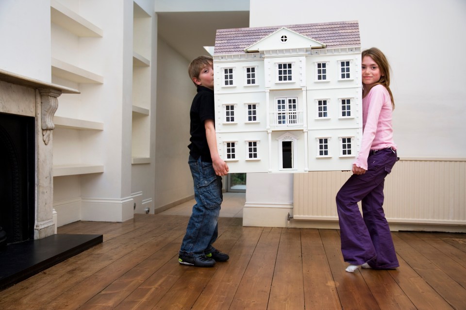 a boy and a girl standing behind a doll house