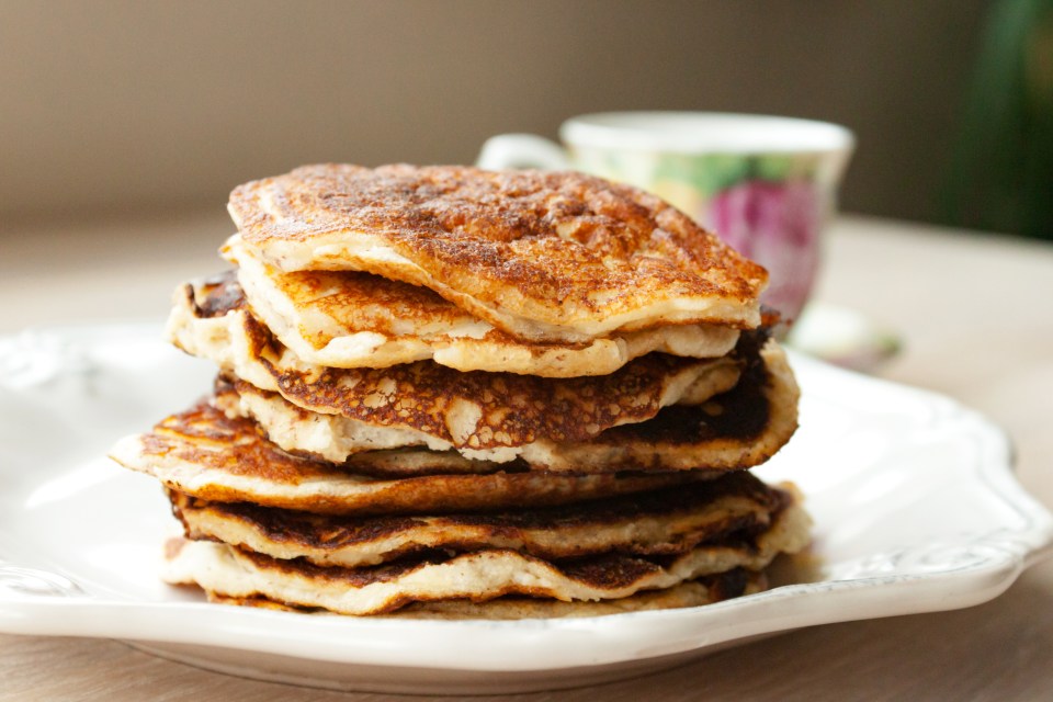 a stack of pancakes on a white plate with a cup in the background