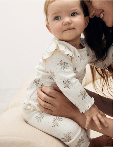 a woman is holding a baby who is wearing a white shirt with flowers on it