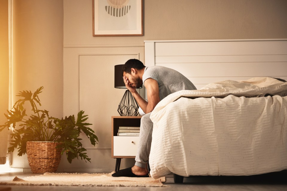 a man sits on a bed with his head in his hands