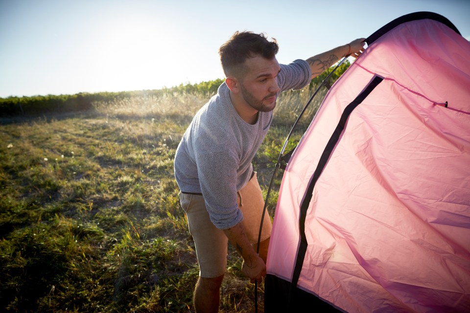 a man is setting up a pink tent in a field