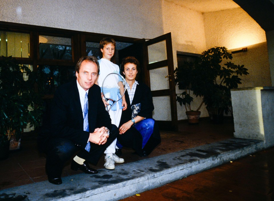 a man and woman kneeling next to a child holding a tennis racket