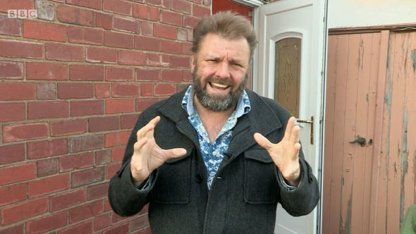 a man with a beard is standing in front of a brick wall making a funny face .