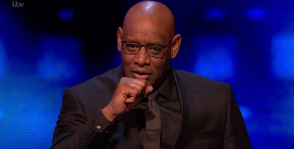 a bald man wearing glasses and a black suit is sitting on a stage .