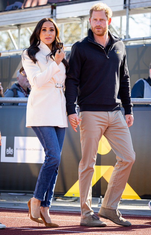 prince harry and meghan markle hold hands while walking on a track