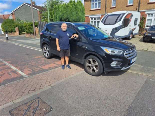 a man is standing next to a black suv on the side of a road .