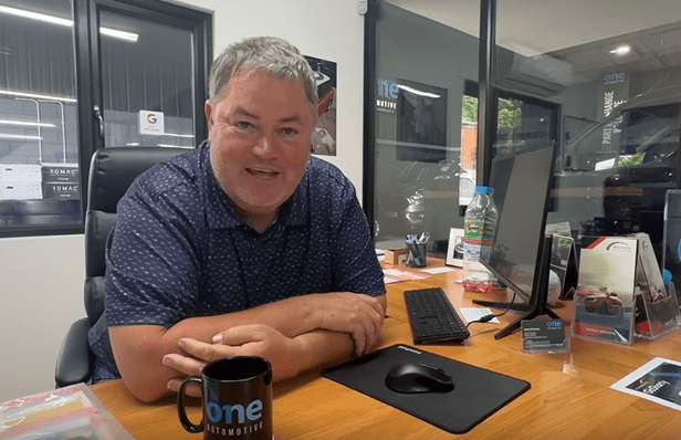 a man sits at a desk with a mug that says one automotive