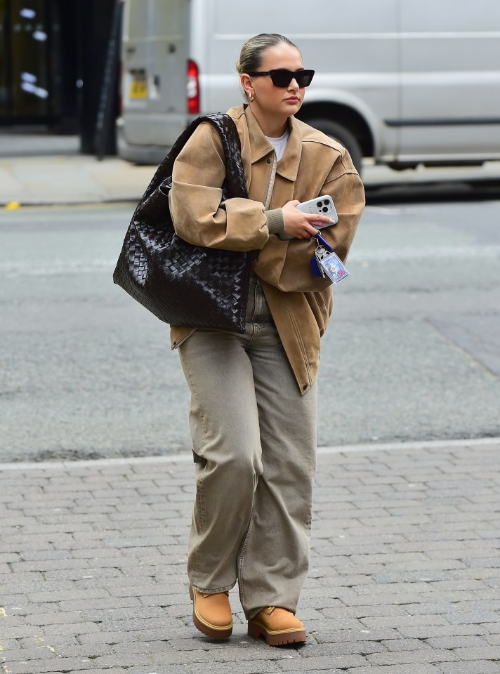 a woman wearing sunglasses and a brown jacket is walking down the street