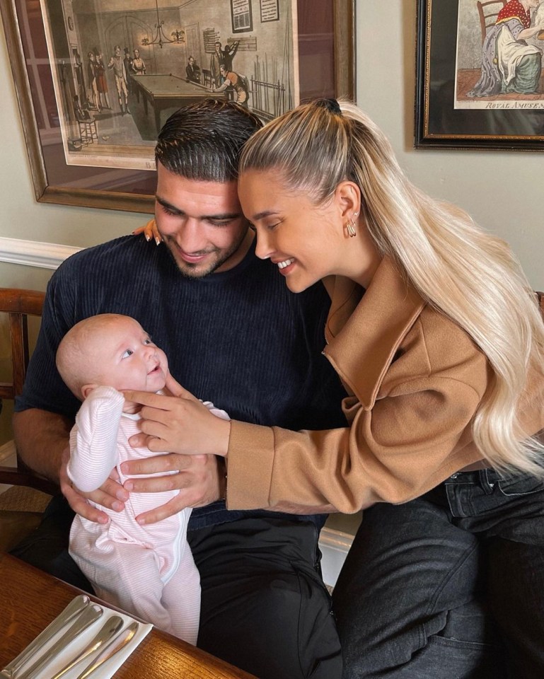 a man and woman holding a baby in front of a framed picture of a pool table