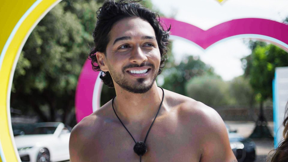 a shirtless man smiles in front of a pink heart