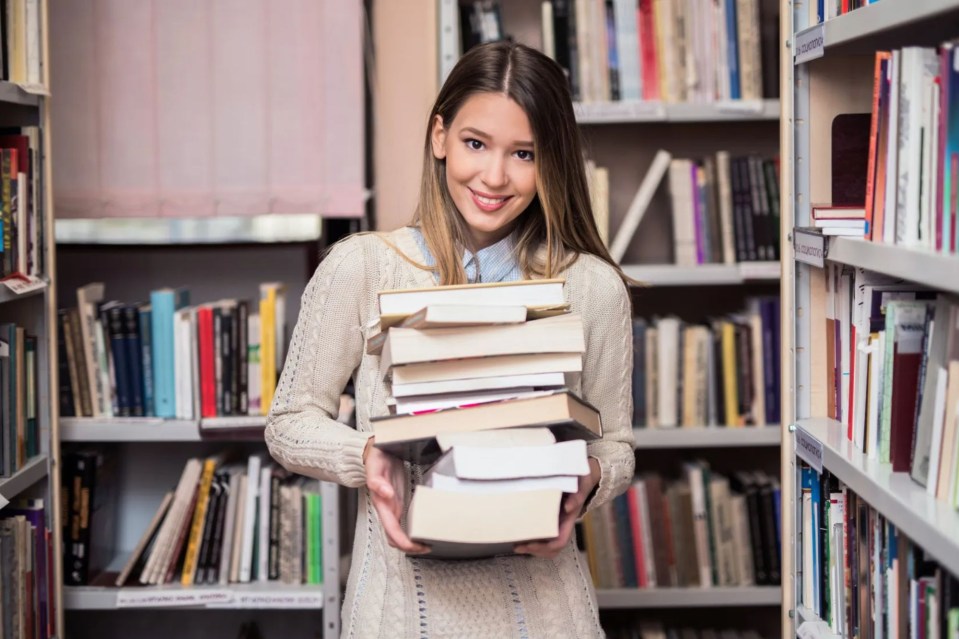 a woman is holding a stack of books in a library