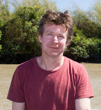 a man in a red shirt stands in front of a body of water