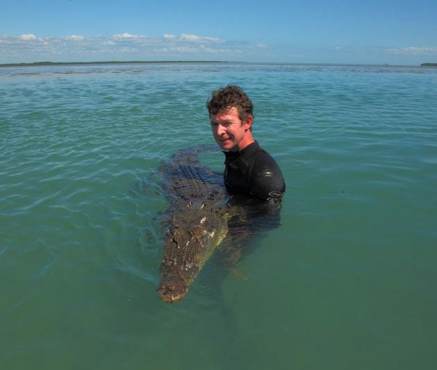 a man in a wetsuit is holding a large crocodile in the water