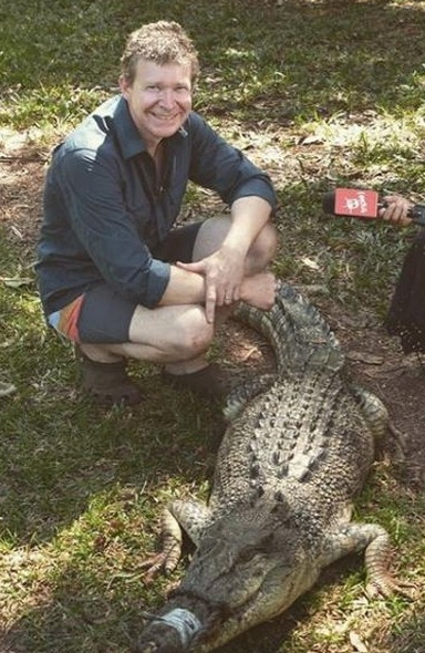 a man is kneeling down next to a large crocodile