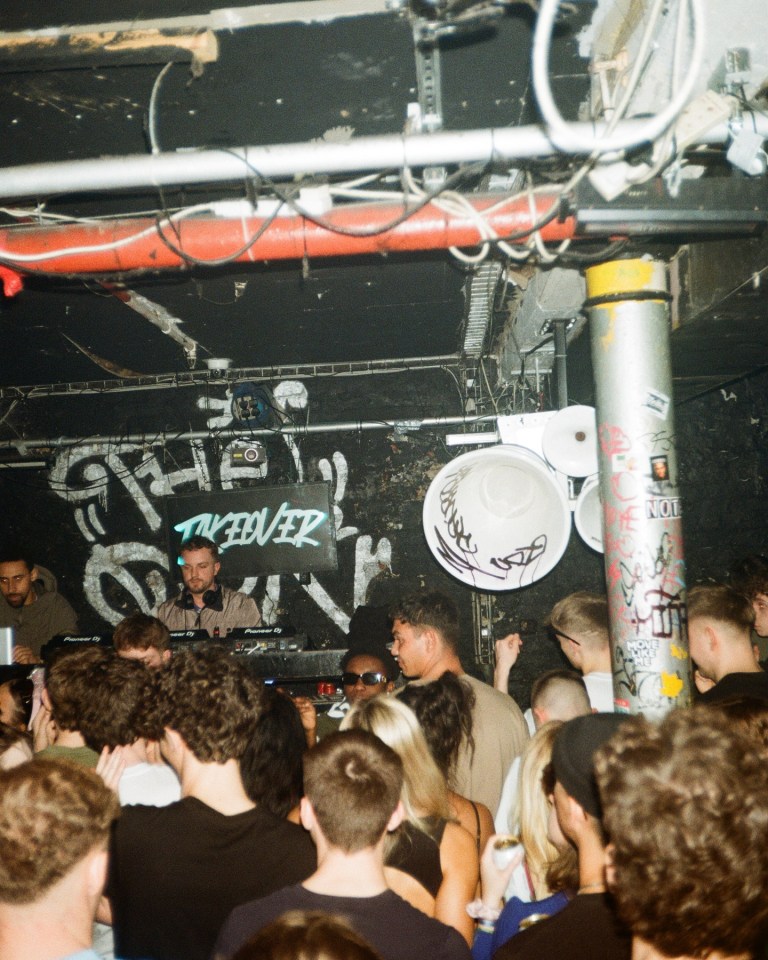 a crowd of people are gathered in a dark room with graffiti on the walls and a dj playing music