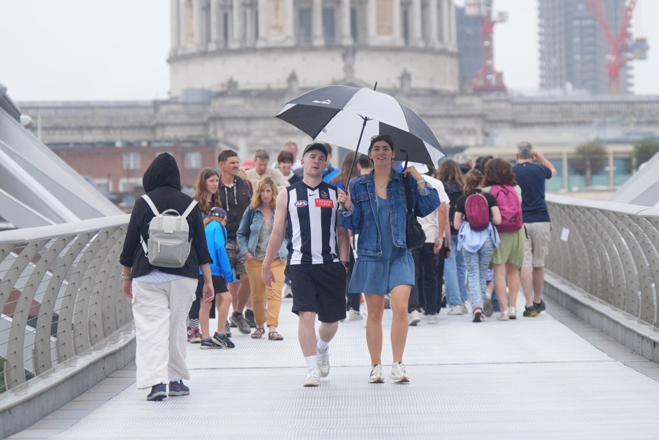 People get caught in a rain shower while crossing the Millennium Bridge in London