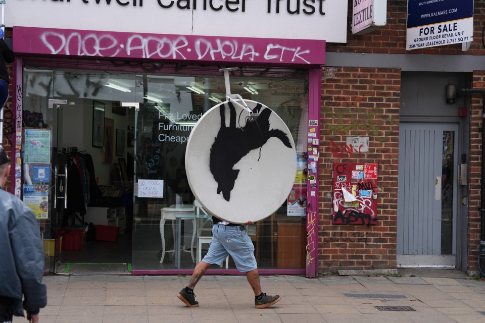 a man is carrying a satellite dish in front of a store called cancer trust