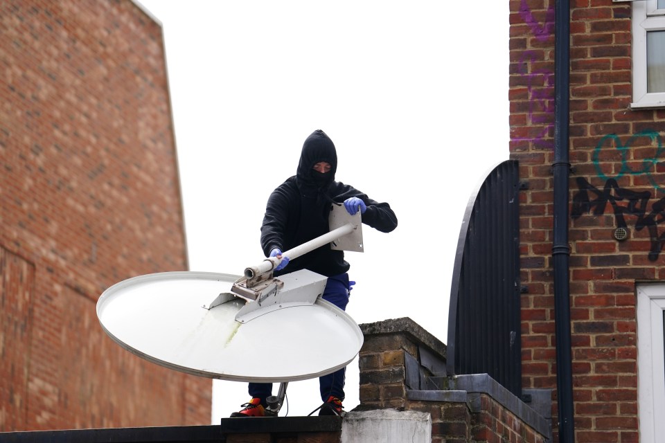 a man in a black hoodie is standing on a roof holding a satellite dish