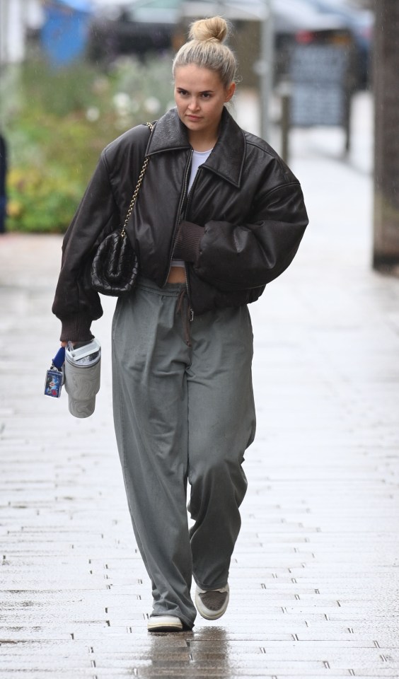 a woman wearing a brown leather jacket and grey pants