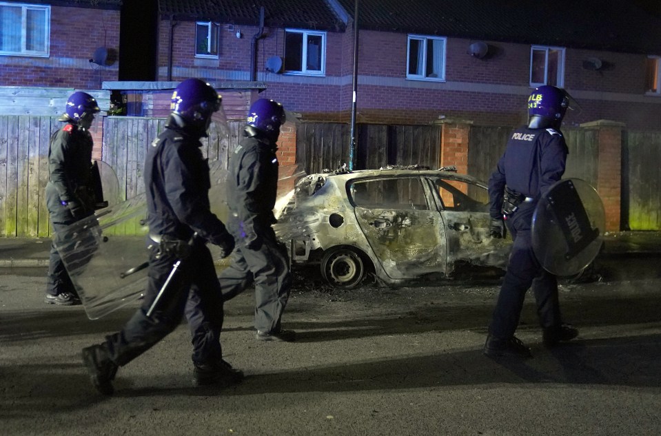 Riot cops walking past the gutted car