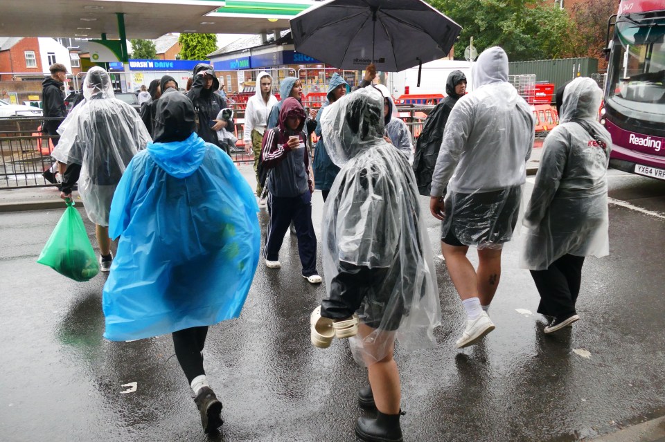 a group of people walking in the rain with a reading bus in the background