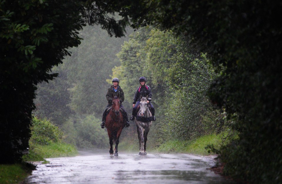 two people riding horses down a road in the rain