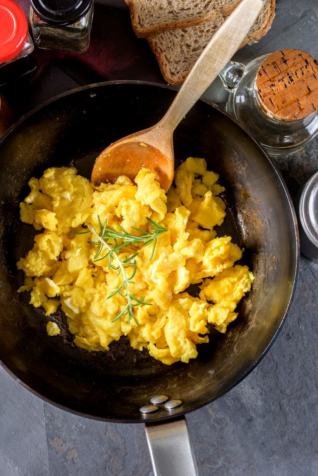 scrambled eggs in a frying pan with a wooden spoon