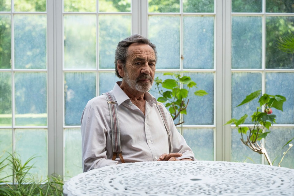 a man with suspenders sits at a table in front of a window