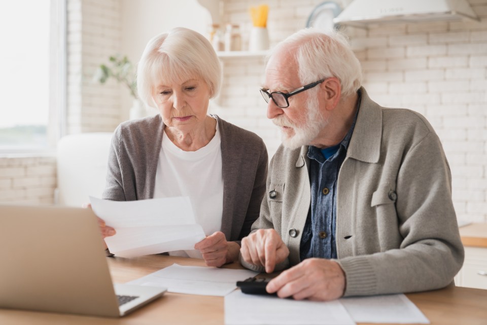 an elderly couple looking at a laptop and a piece of paper