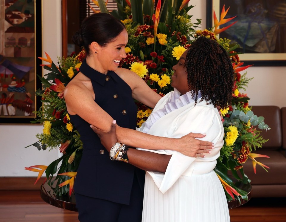 two women hugging in front of a flower arrangement