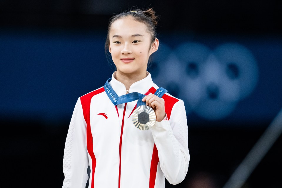 a woman in a red and white jacket is holding a silver medal