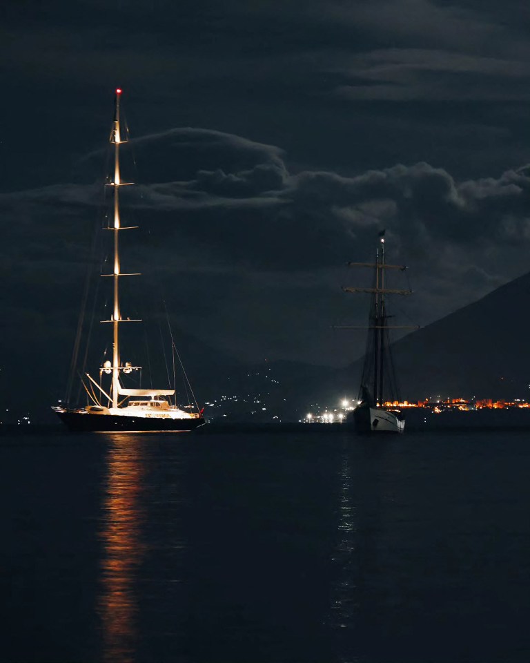 two sailboats in the water at night with mountains in the background