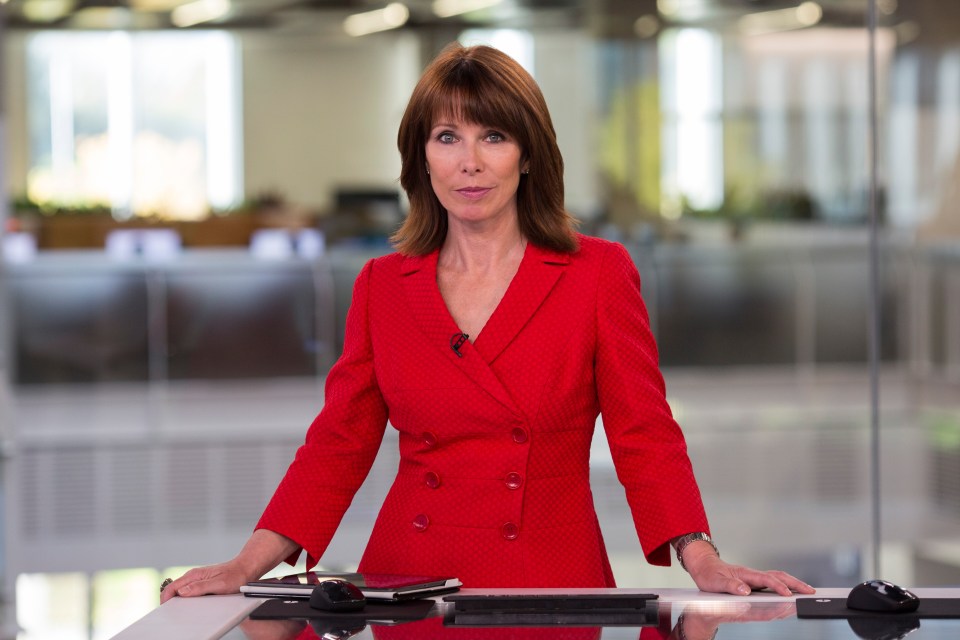 a woman in a red suit is leaning on a desk