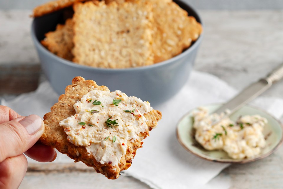 a person is holding a cracker with cheese spread on it