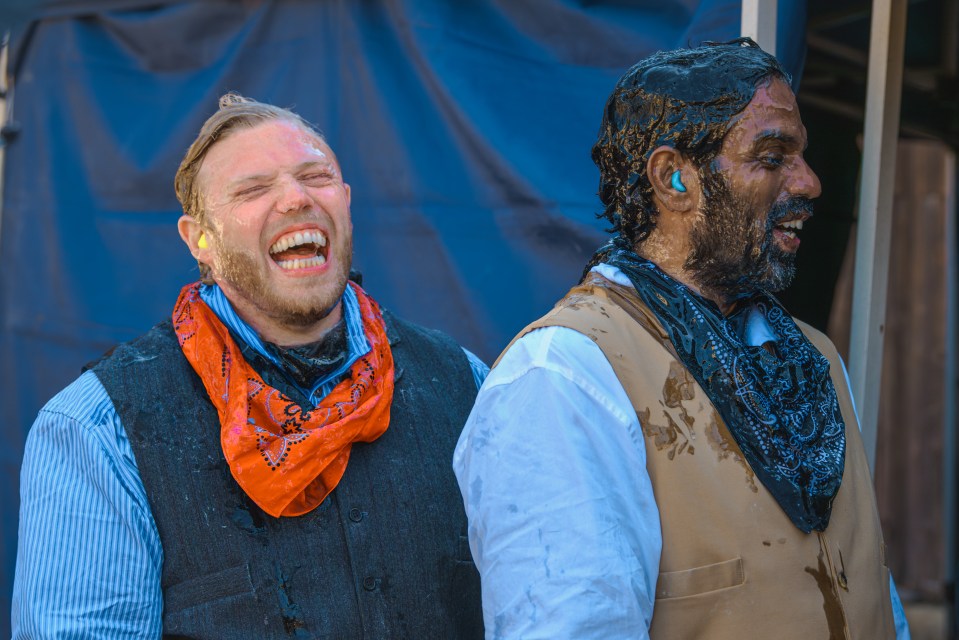 a man wearing an orange bandana is laughing next to another man covered in mud