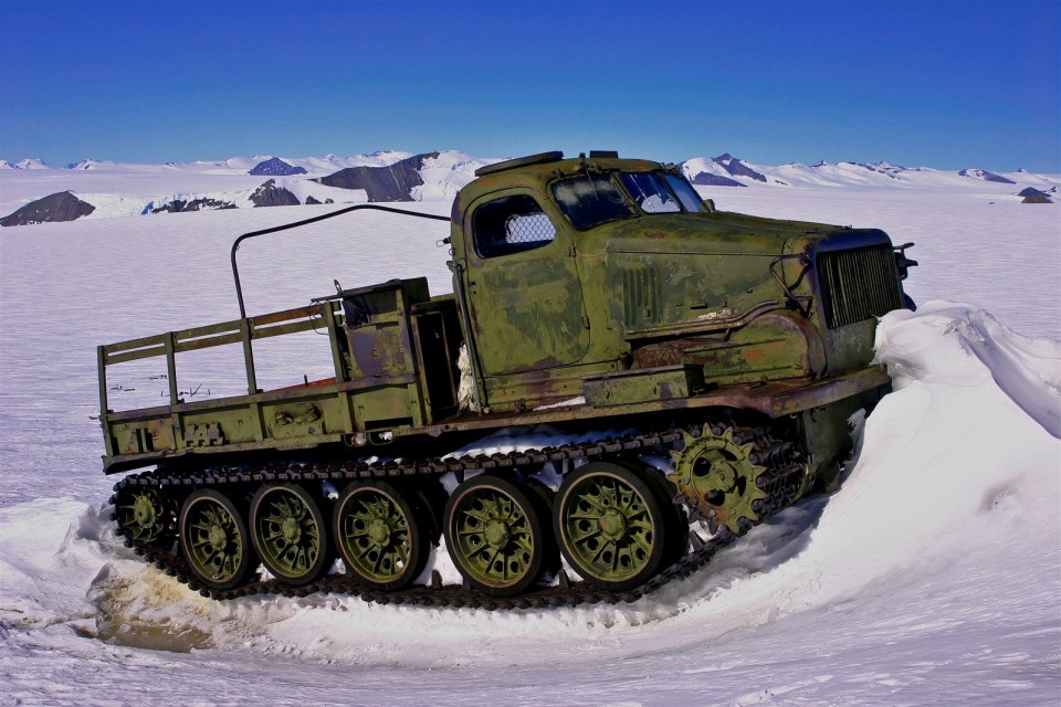 a green military vehicle is driving through the snow