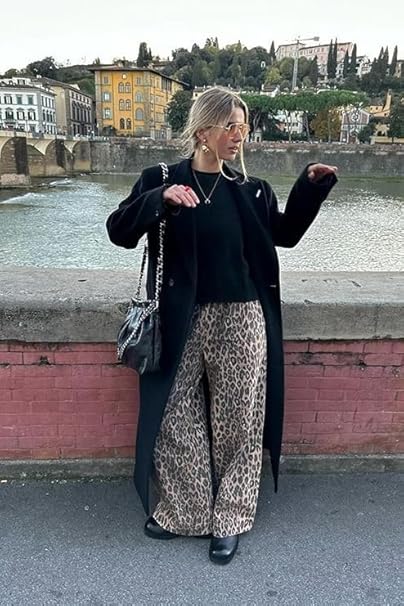 a woman wearing a black coat and leopard print pants is standing on a bridge .