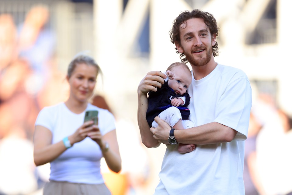 a man holds a baby in his arms while a woman looks on