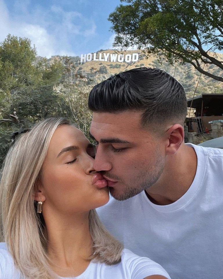 a man and woman kiss in front of the hollywood sign