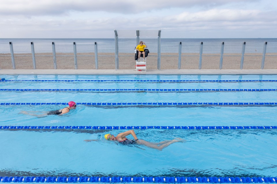 a lifeguard watches two swimmers in a swimming pool