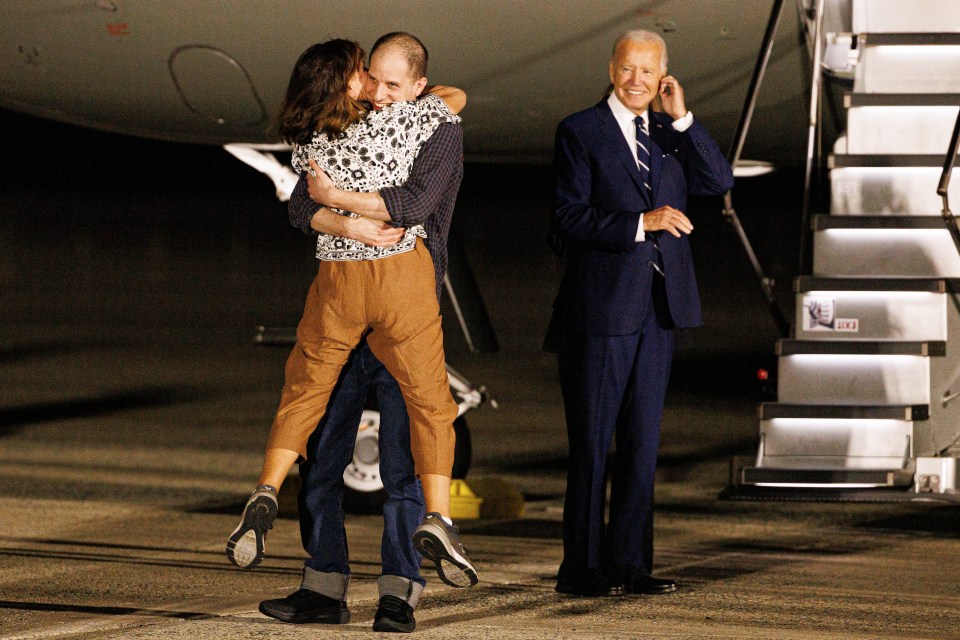 a man in a suit talks on a cell phone while a woman hugs him