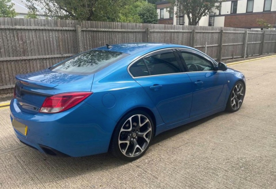 a blue car is parked in front of a wooden fence