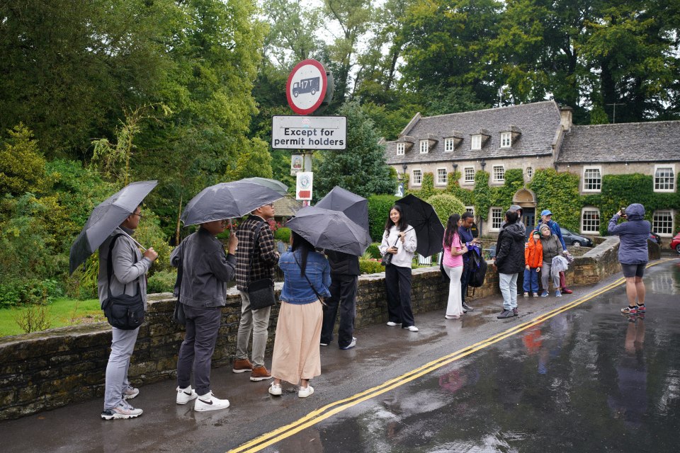 Visitors shelter under umbrellas in the rainy weather at Bibury village in Gloucestershire