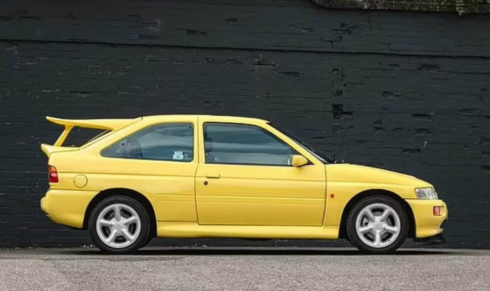 a yellow car is parked in front of a black brick wall .