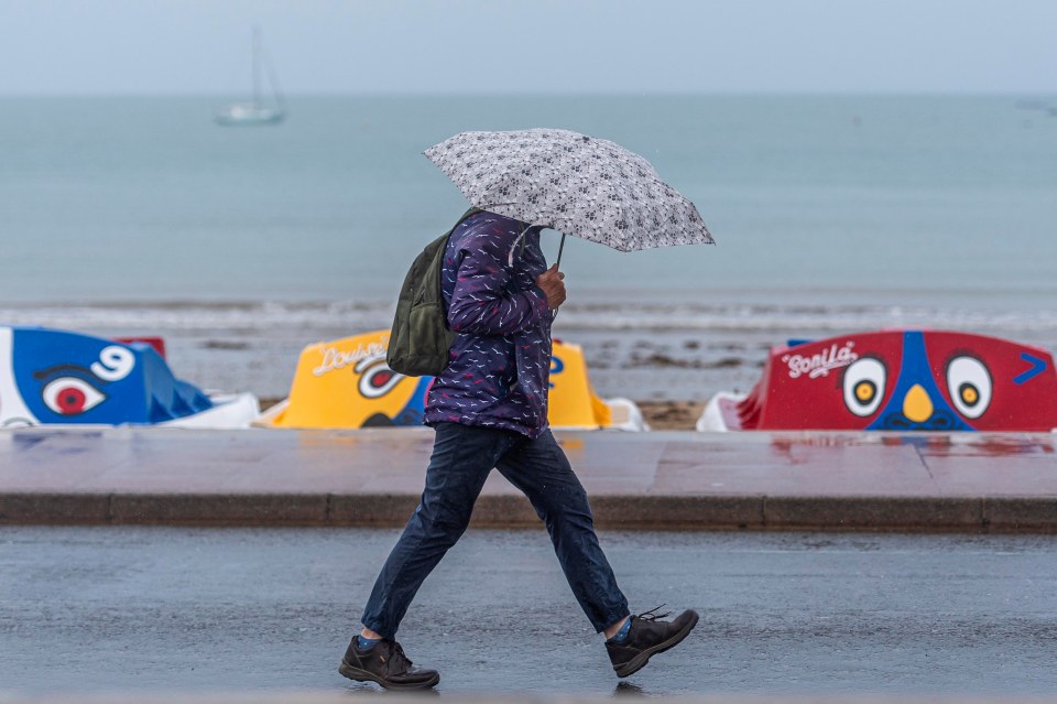 A woman shelters under an umbrella in Swanage, Dorset, as the August bank holiday gets off to a wet start